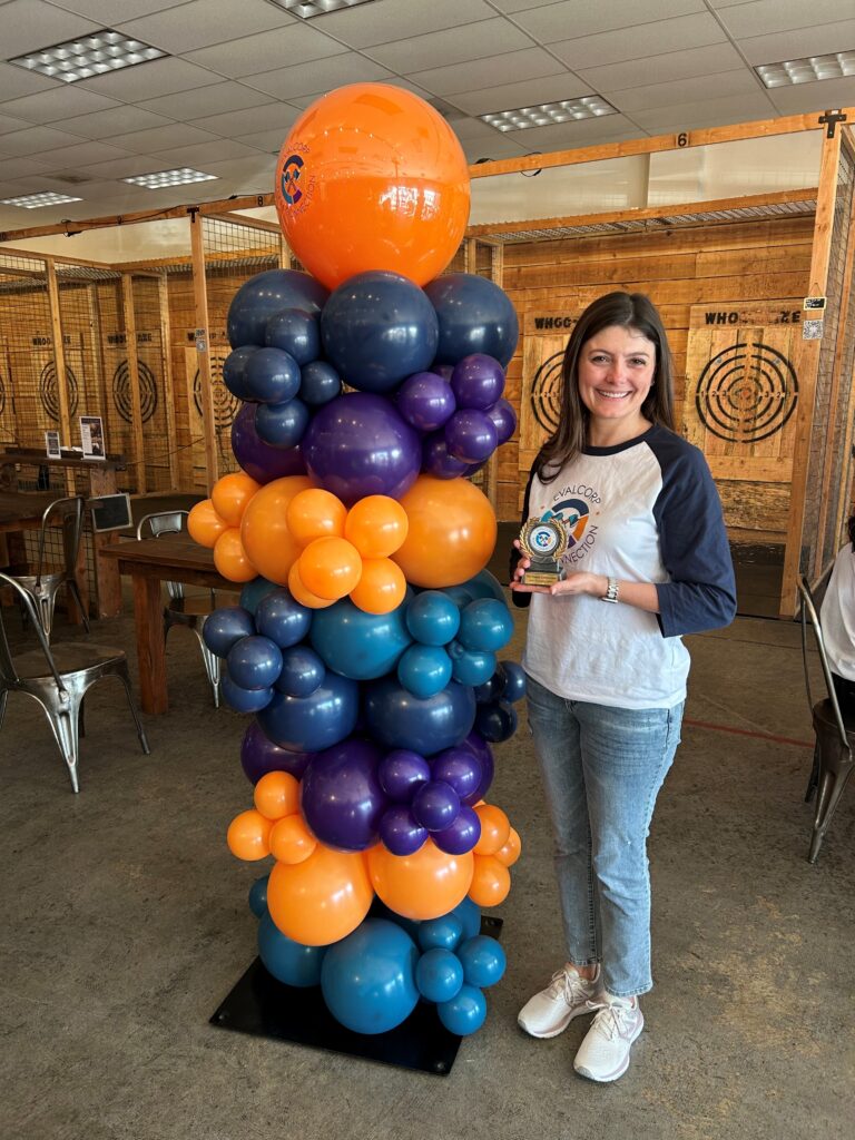 Allison smiles with her trophy next to the balloon arch