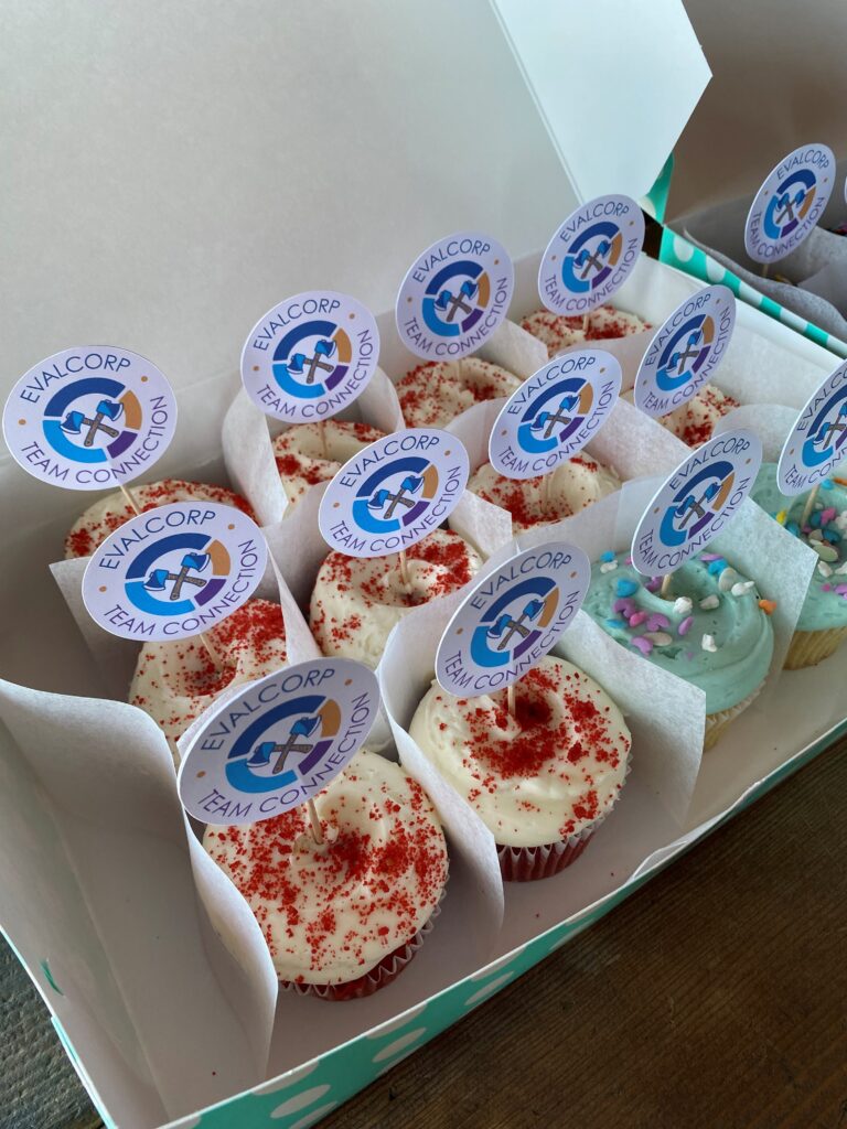 A box of a dozen cupcakes with sticks that have the logo for "EVALCORP Team Connection"