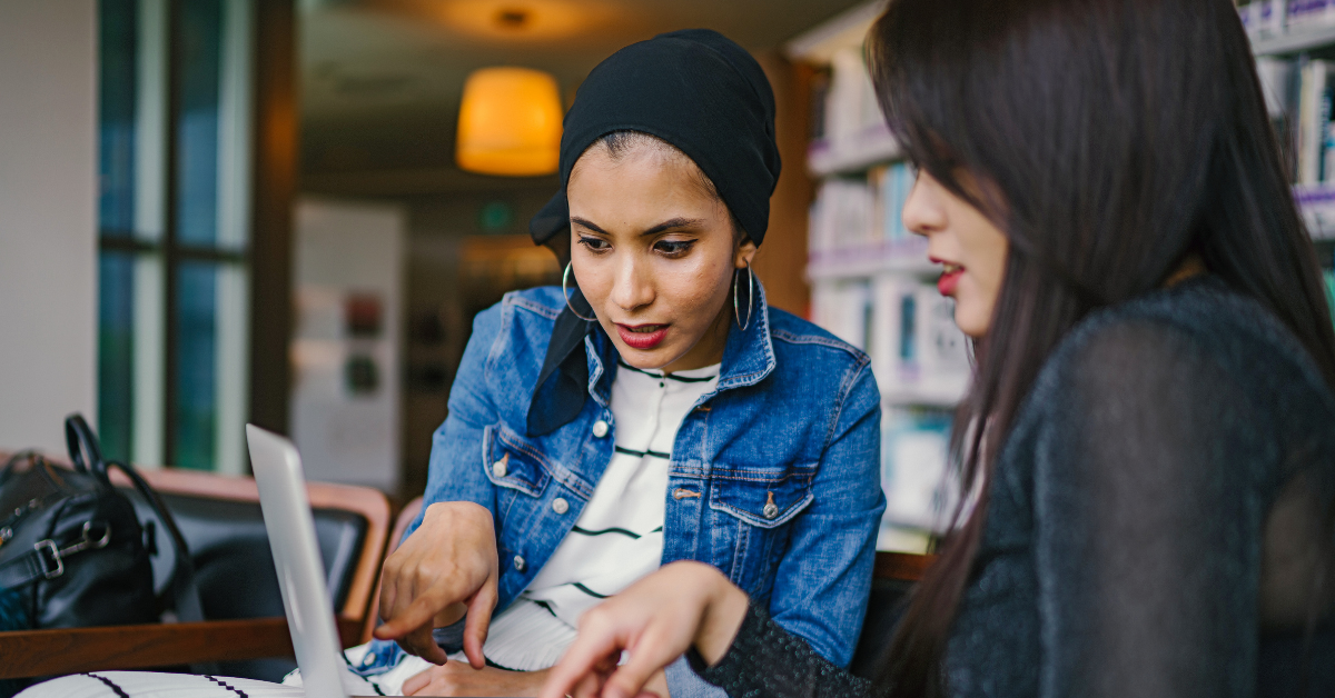 Two women sitting down and pointing at a laptop screen together looking focused